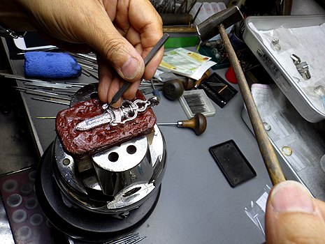 職人がクロムハーツのシルバーアイテムに専用工具でダイヤモンドを石留めしている作業風景